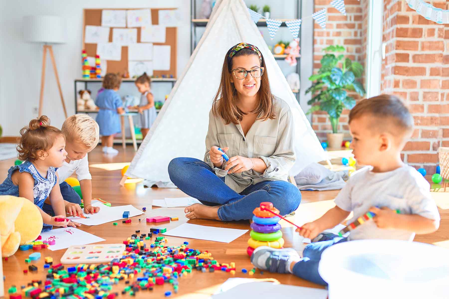 A childcare provider seated with toddlers during drawing and playtime A childcare provider seated with toddlers during drawing and playtime