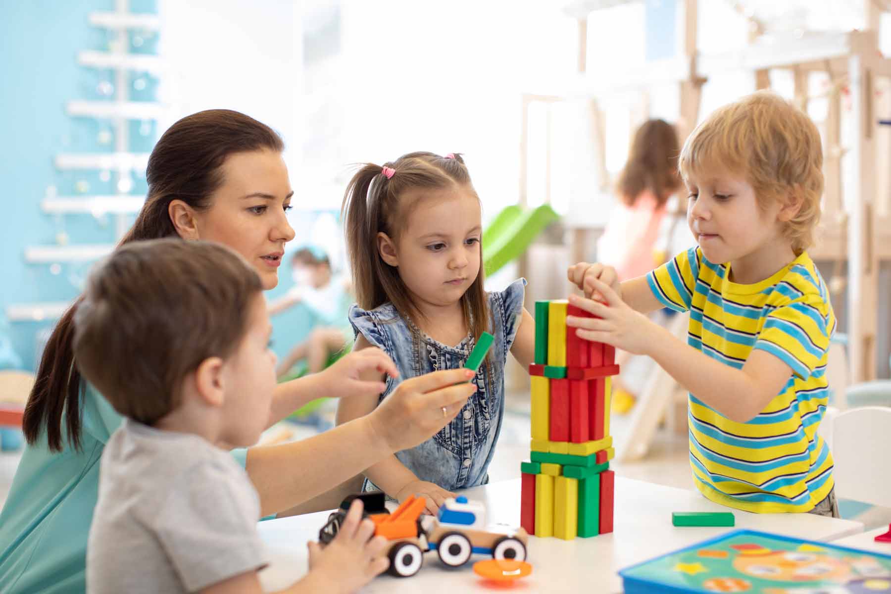 Toddlers in a daycare playing with colorful blocks while a teacher helps Toddlers in a daycare playing with colorful blocks while a teacher helps