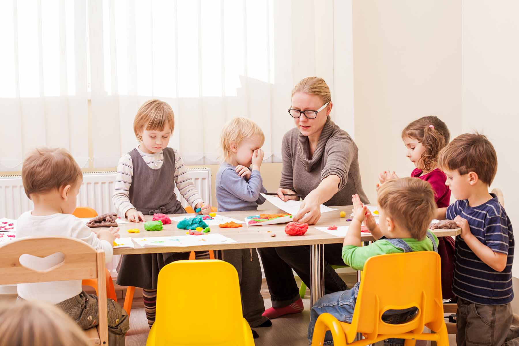 A daycare teacher guides a group of young children as they work on a colorful clay activity A daycare teacher guides a group of young children as they work on a colorful clay activity