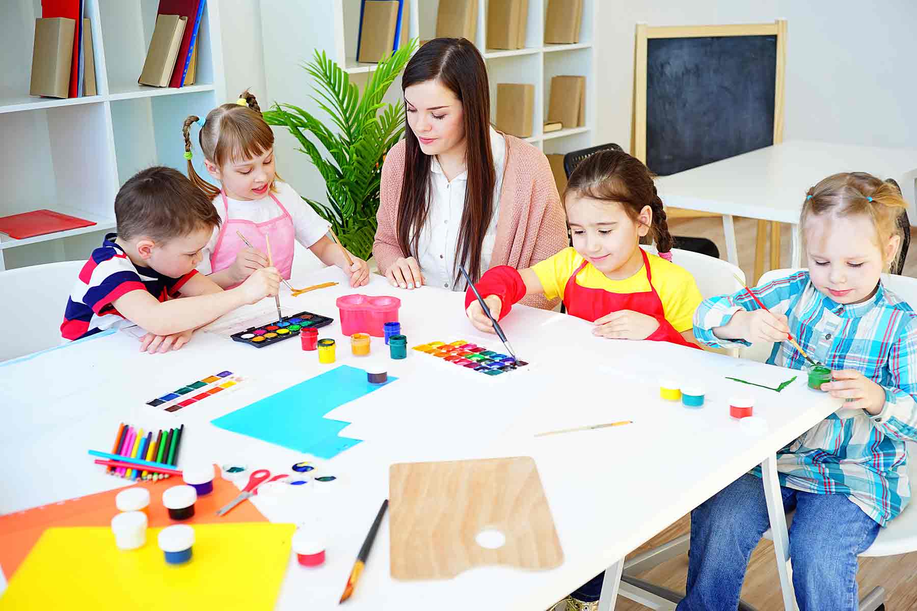 Daycare teacher assisting young children during painting activity in a classroom