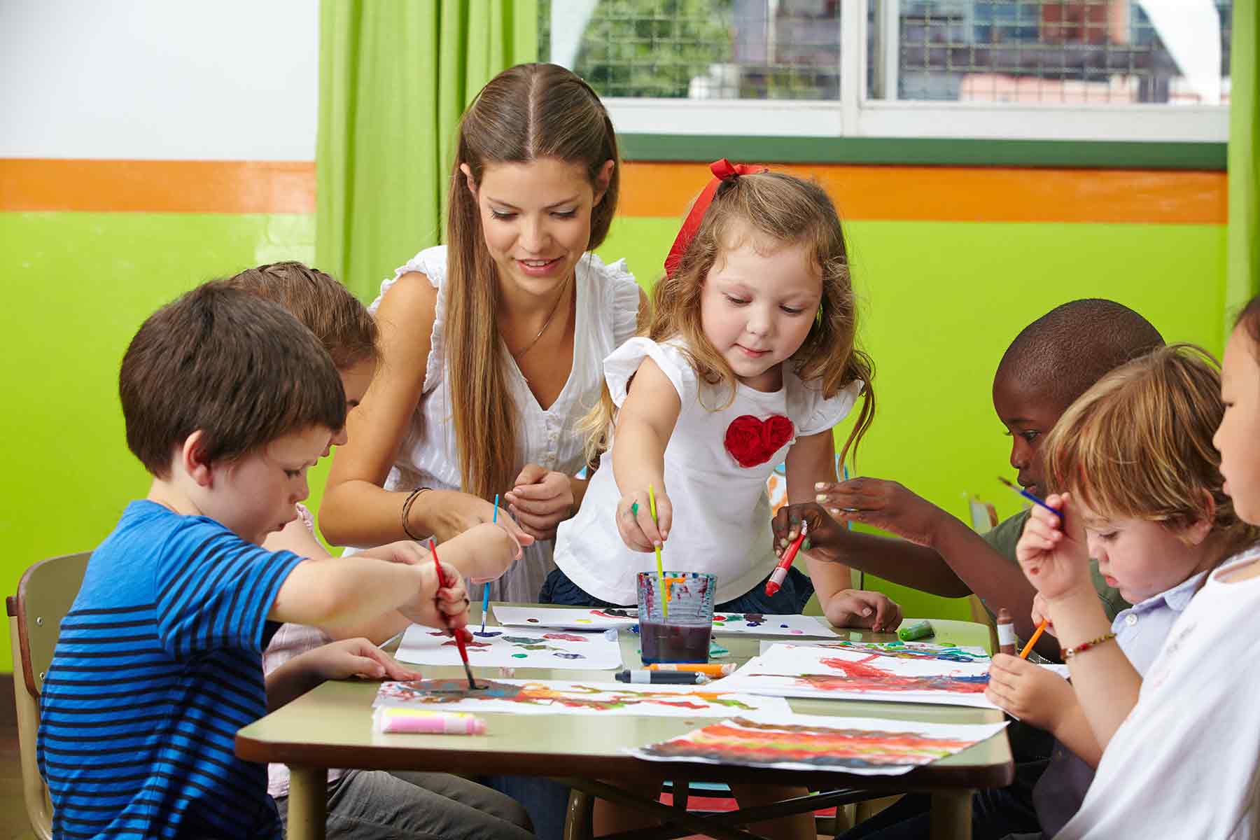 A daycare teacher assisting a group of children with a painting activity