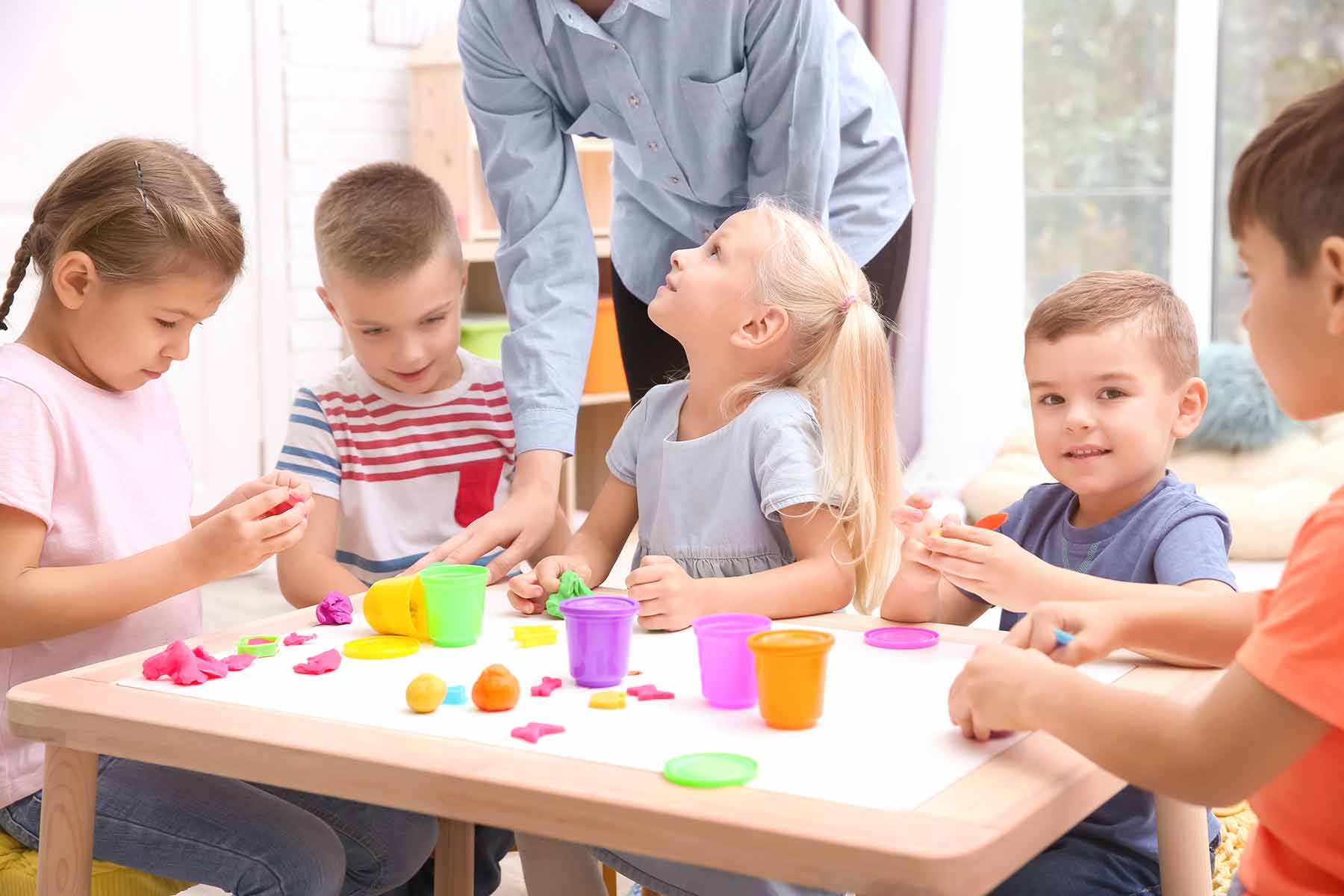 A group of children happily working on a play dough modeling activity with their teacher 