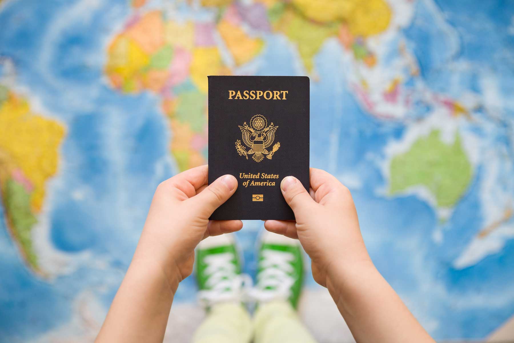 A child holding a passport and standing on a map of the world