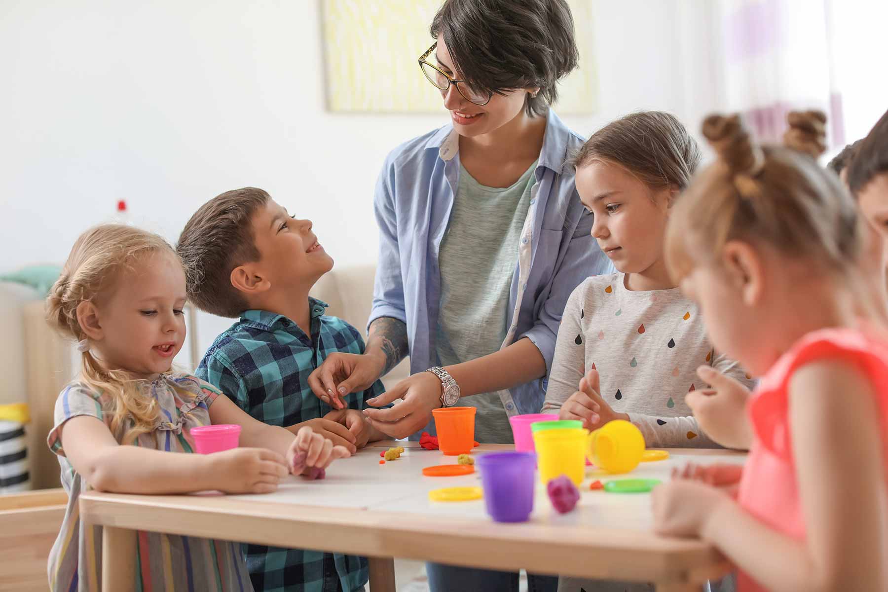 A daycare teacher engaging a group of young children in clay modeling activities
