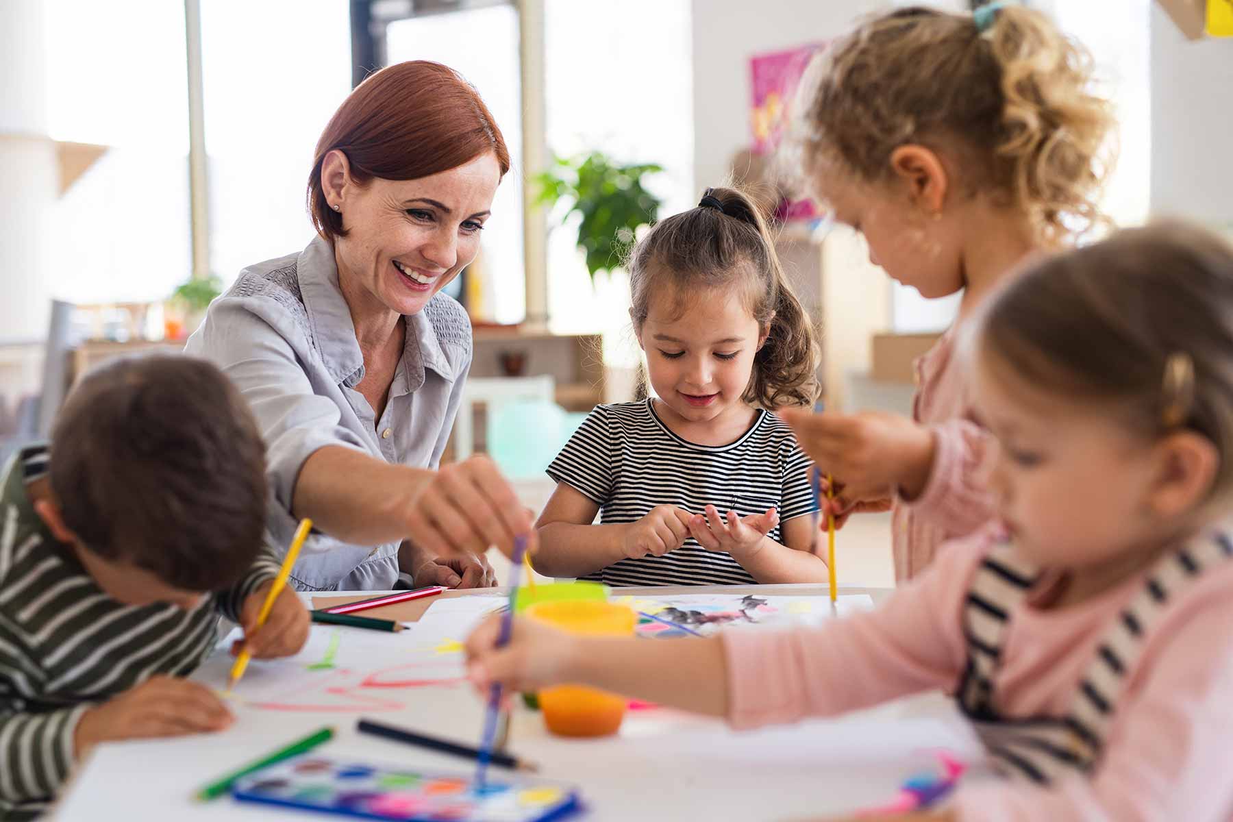Group of small nursery school children enjoying art activity with teacher