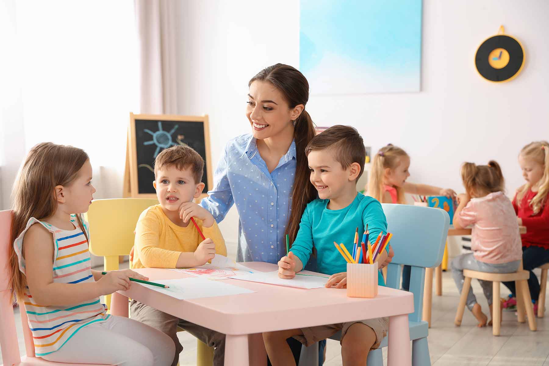 Teacher assists young learners during an arts and crafts session at a daycare Teacher assists young learners during an arts and crafts session at a daycare