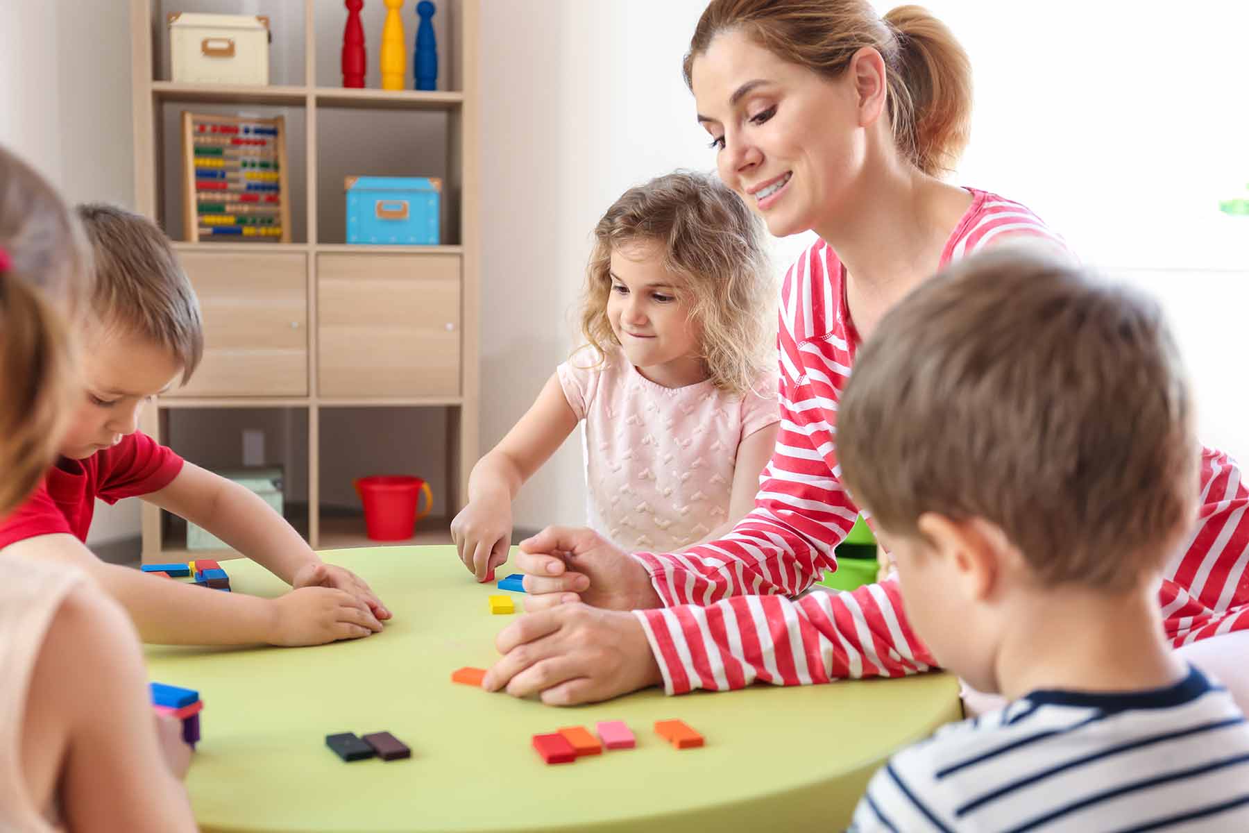 Daycare teacher playing with children using colorful educational building blocks