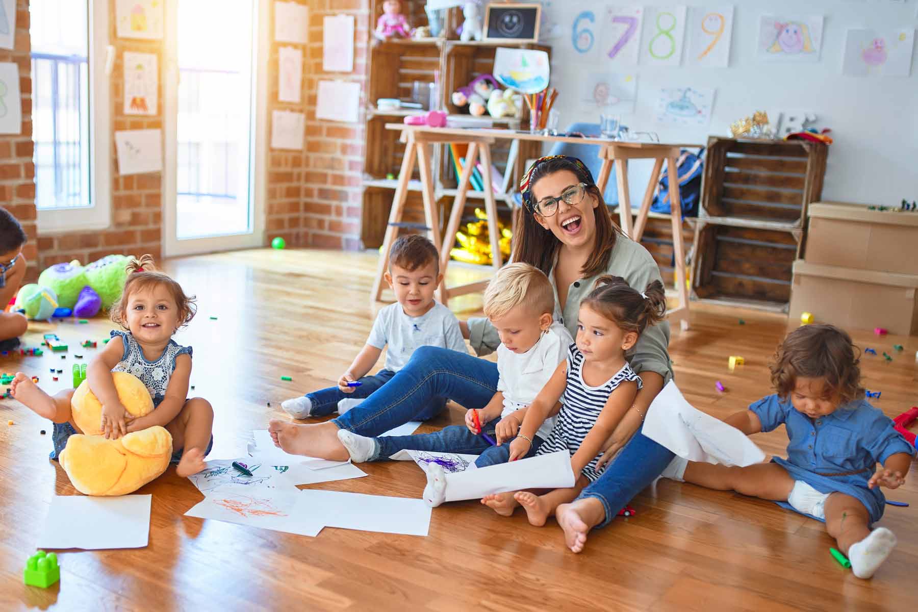 A daycare teacher sitting on the floor with a group of toddlers at a childcare center A daycare teacher sitting on the floor with a group of toddlers at a childcare center