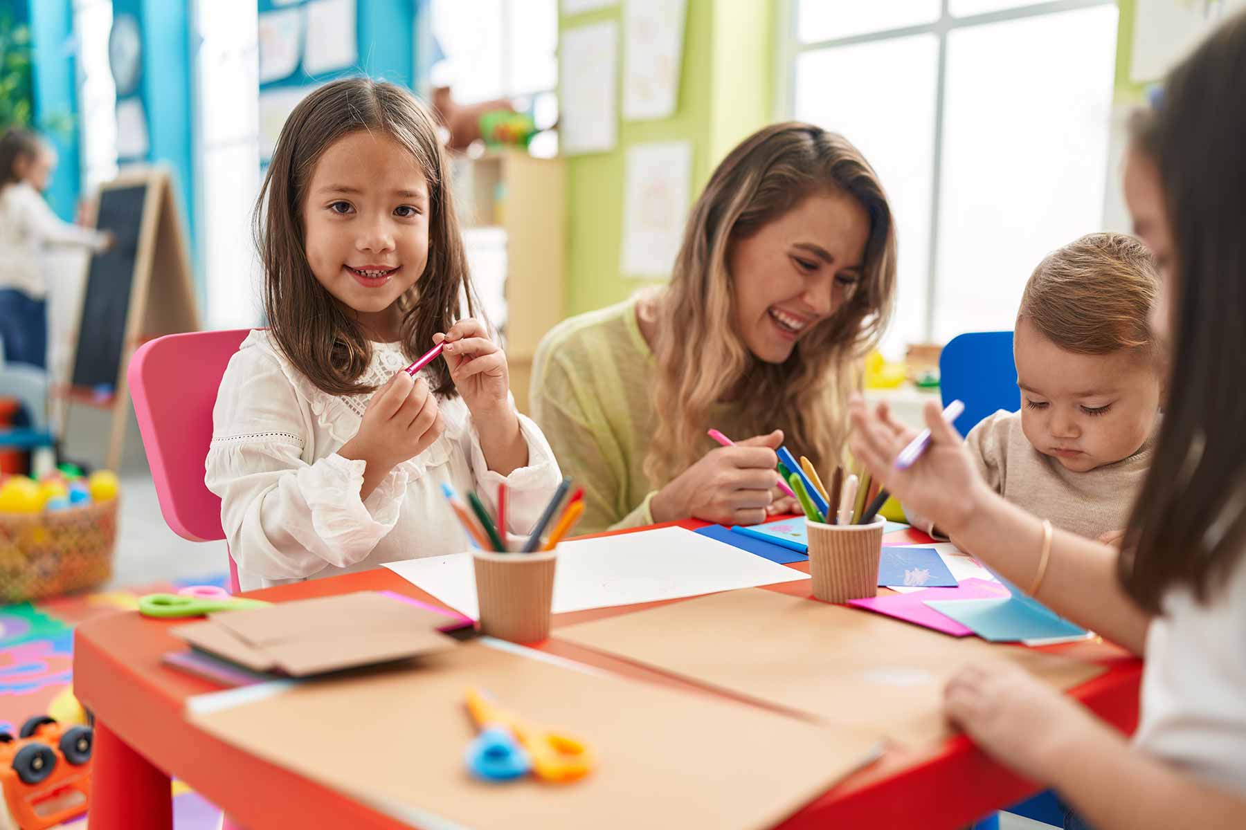 A daycare teacher and group of children enjoying a drawing activity together