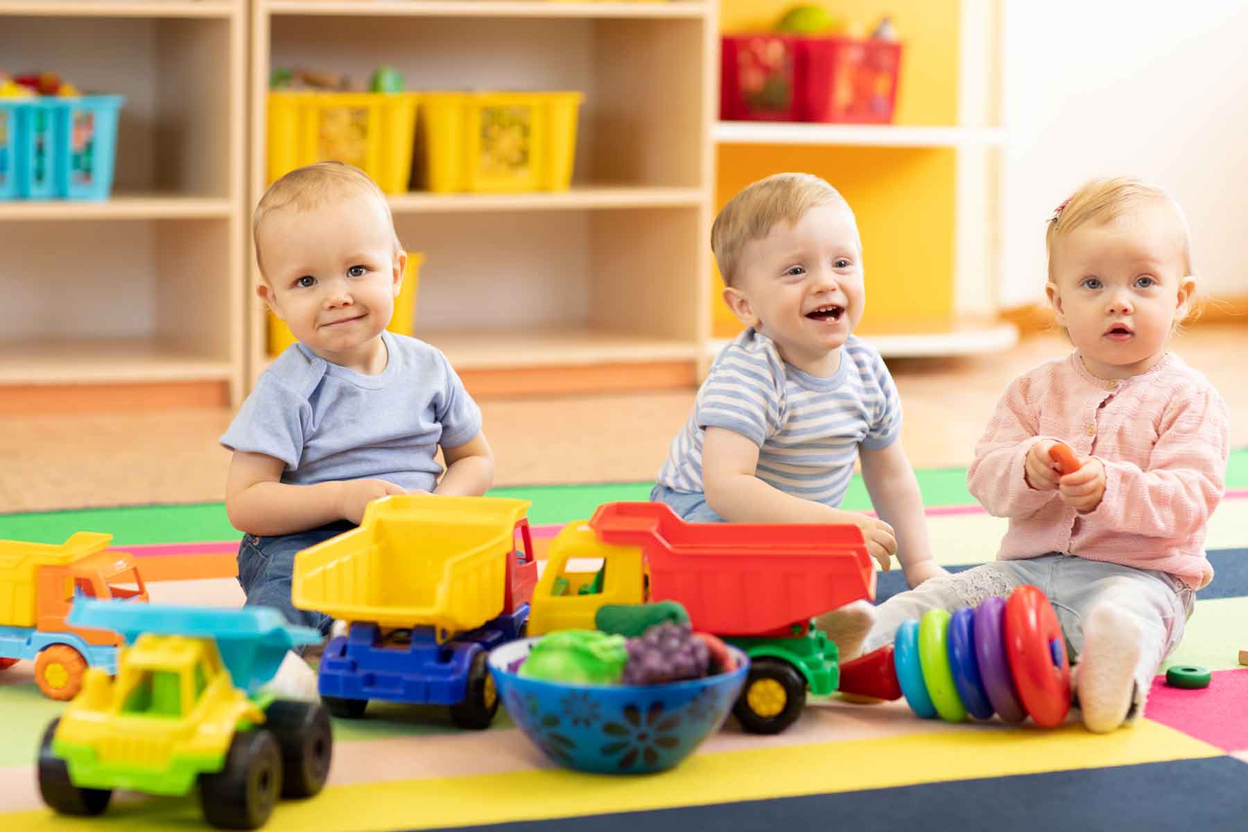 Three infant children playing with colorful toy trucks at a daycare Three infant children playing with colorful toy trucks at a daycare