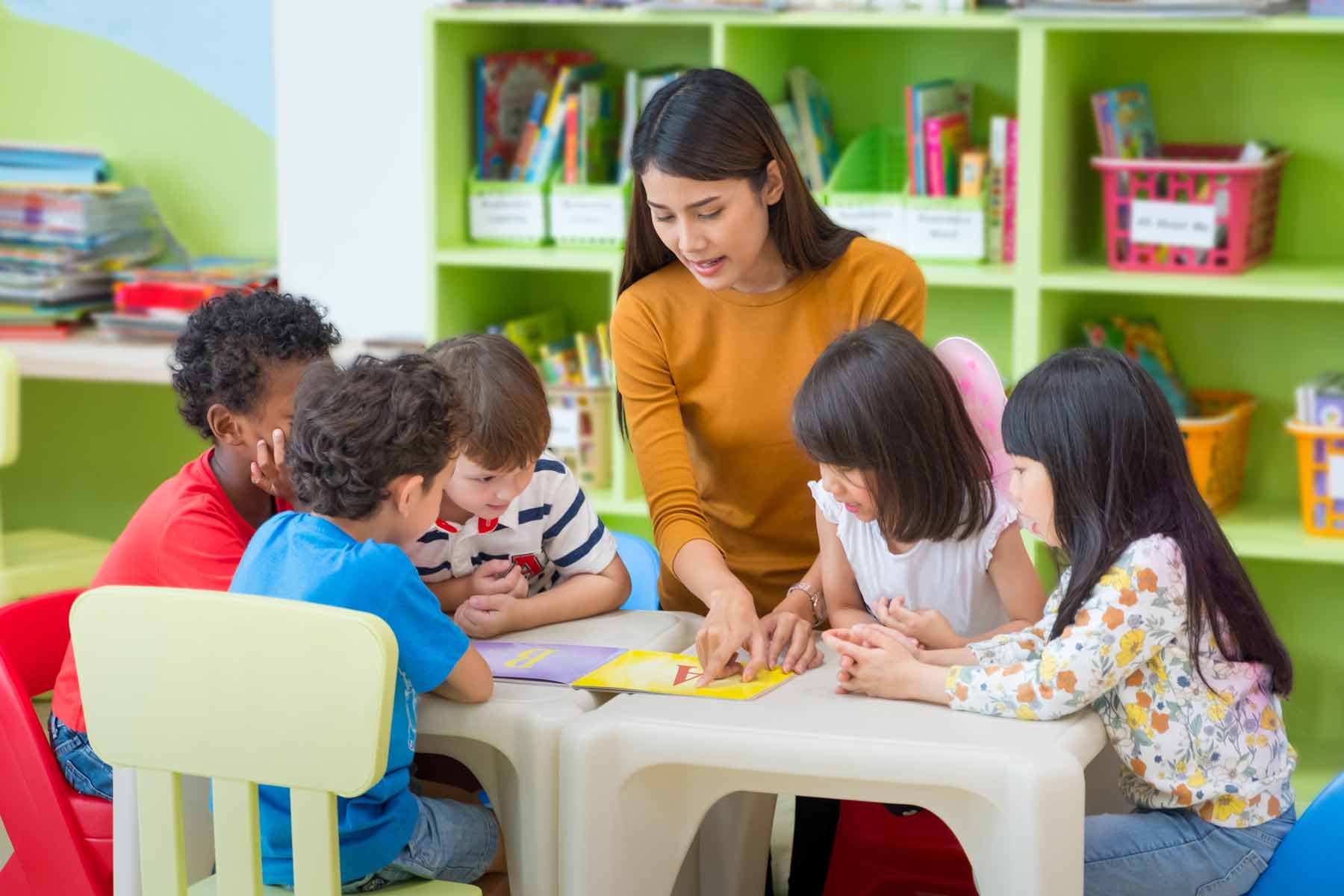 A kindergarten teacher showing children a book with the alphabet.