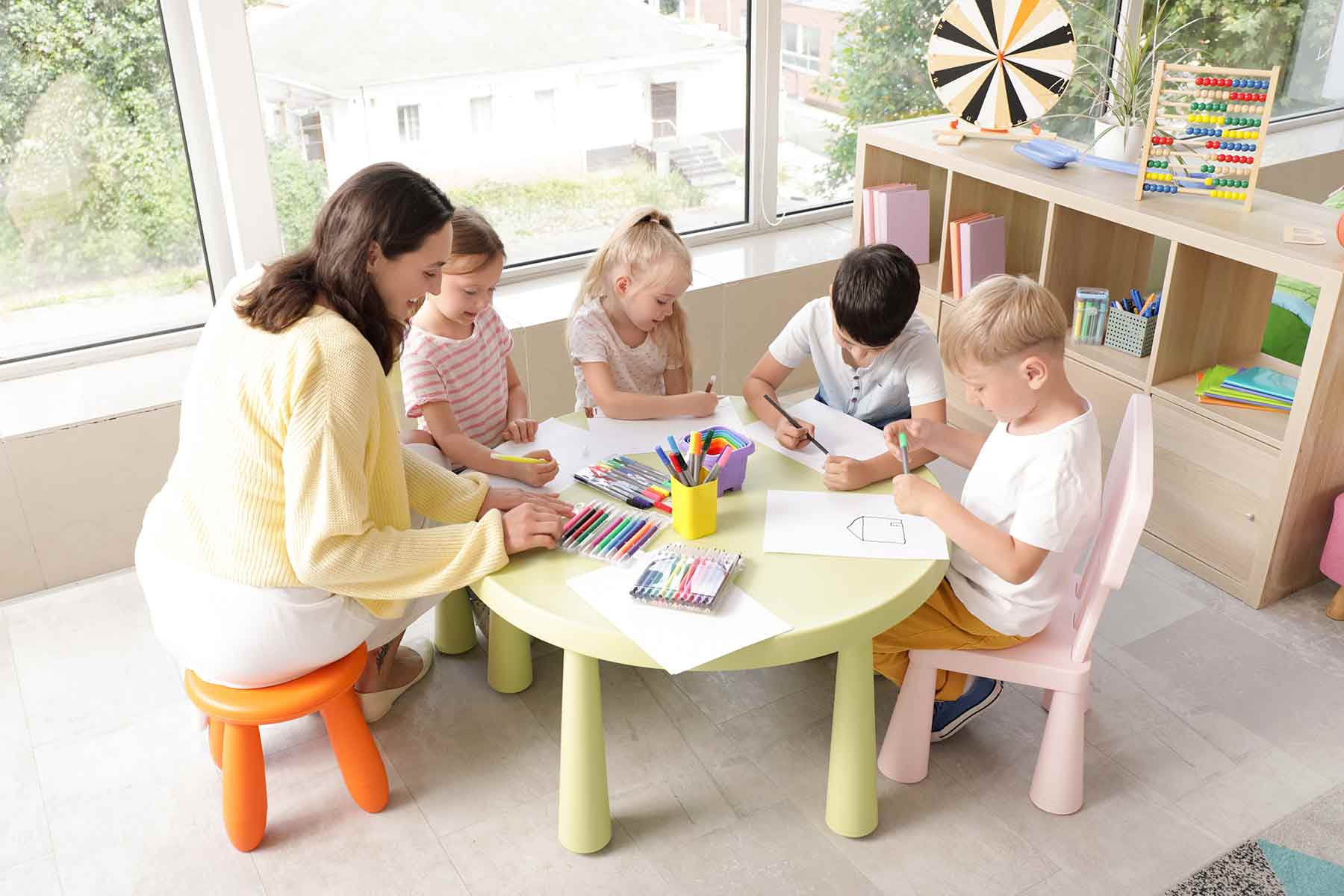 Little children with their daycare teacher drawing at a table Little children with their daycare teacher drawing at a table