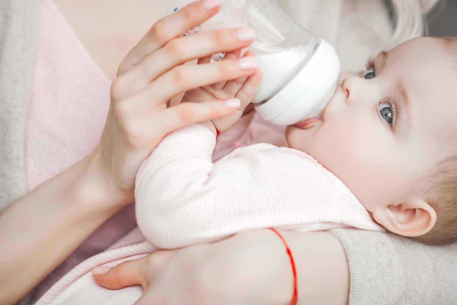 A mother feeding her baby formula in a bottle.