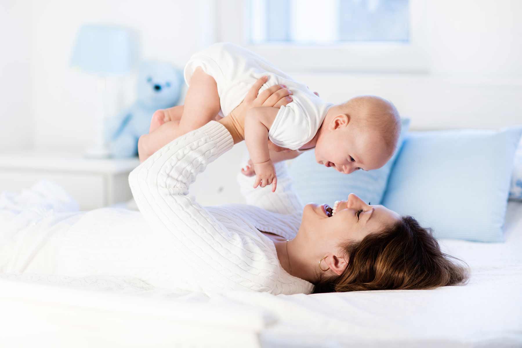 A mother holding her baby while lying on a bed