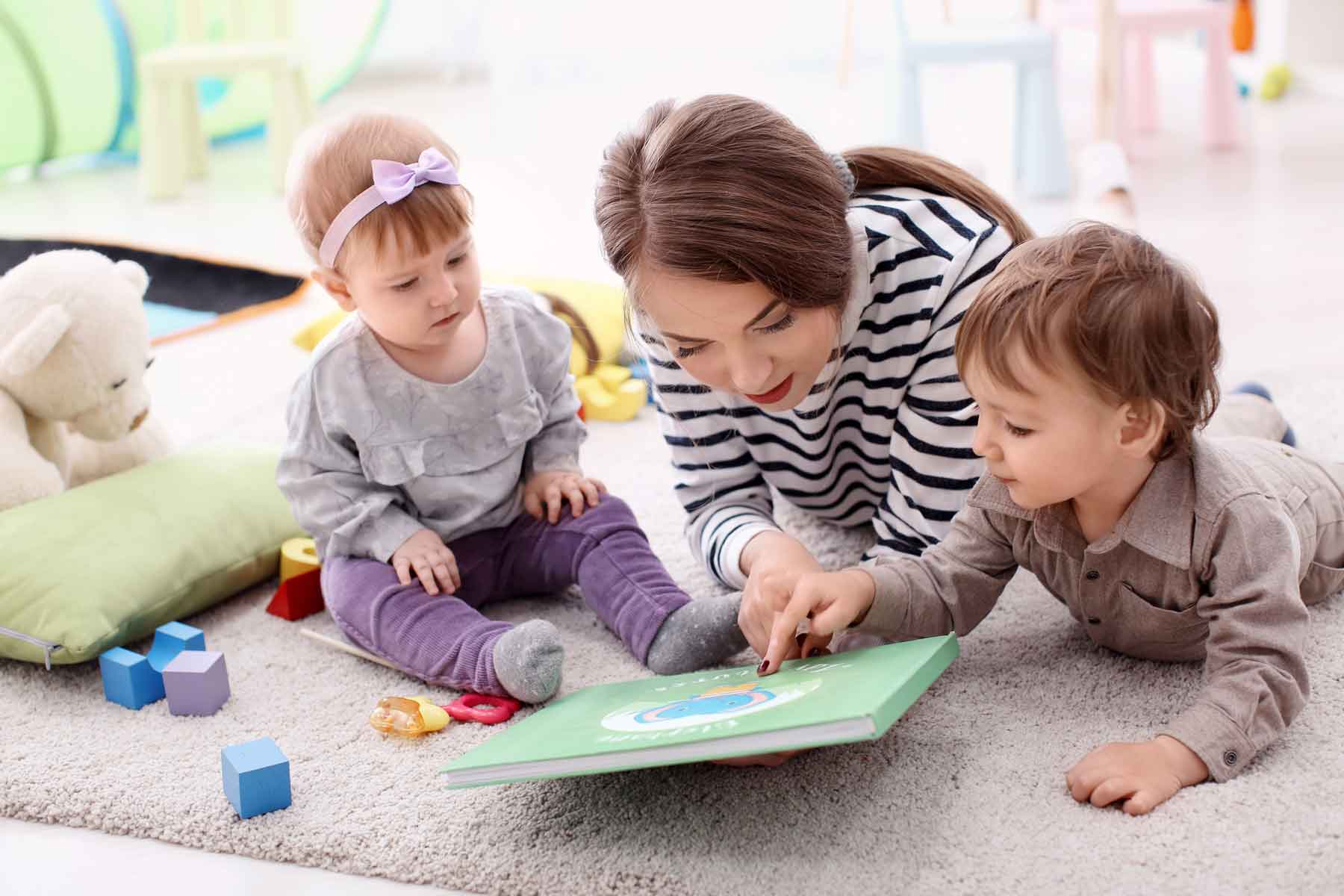 A nanny reading a book to two young children.