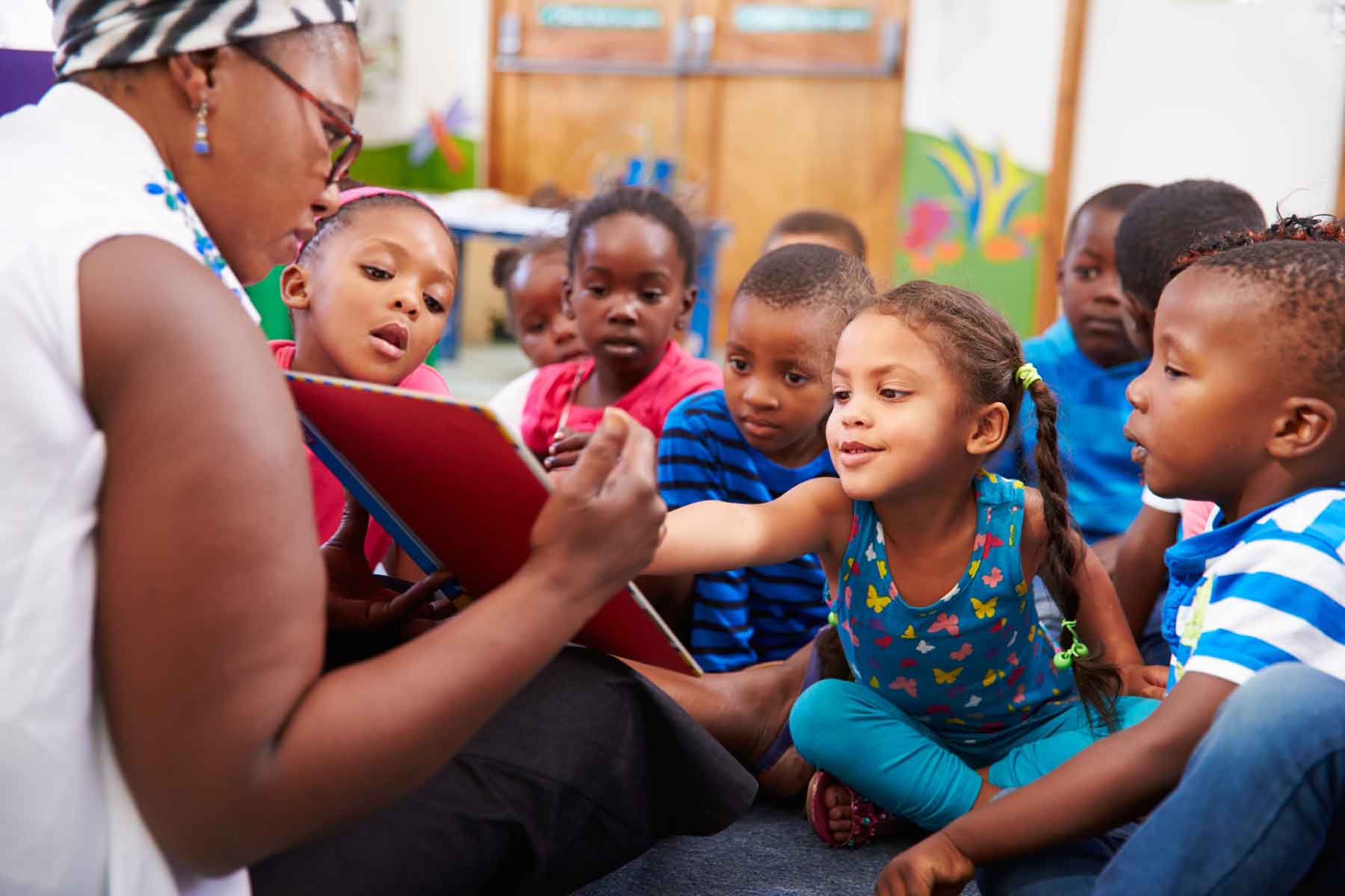 A teacher reading a book to children in pre-kindergarten (pre-K)